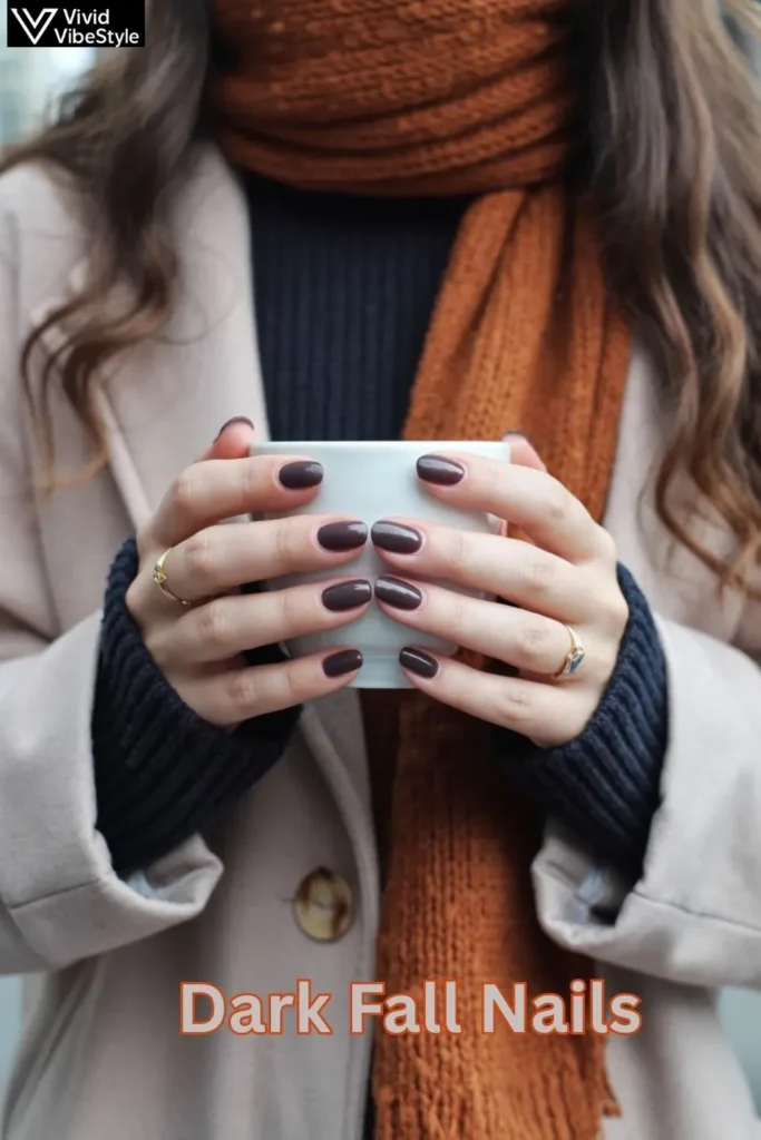A stylish woman with espresso-toned dark fall nails holds a warm coffee cup, her outfit layered in autumn textures and tones that perfectly complement her manicure.
