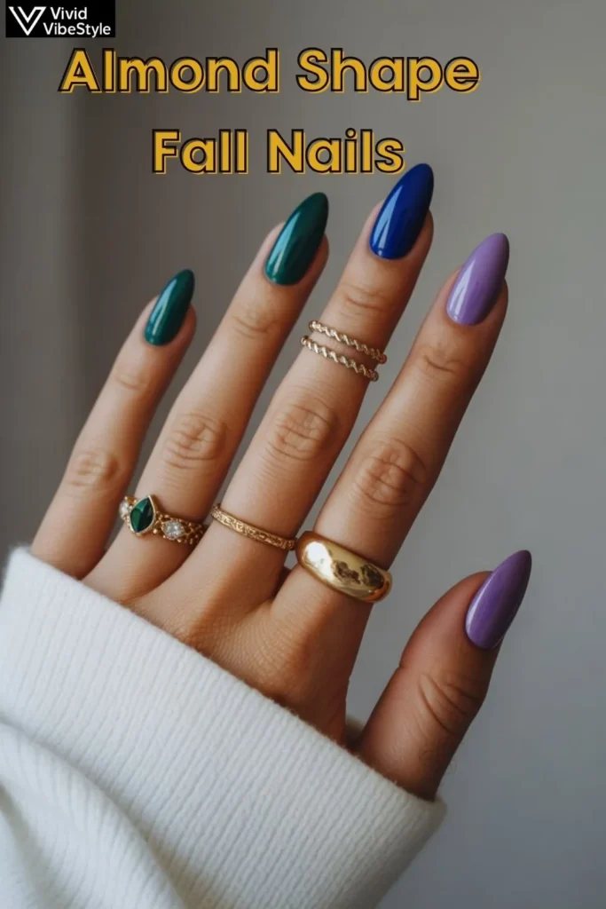 Almond shape fall nails in jewel tones emerald green, sapphire blue, and amethyst purple with gold rings