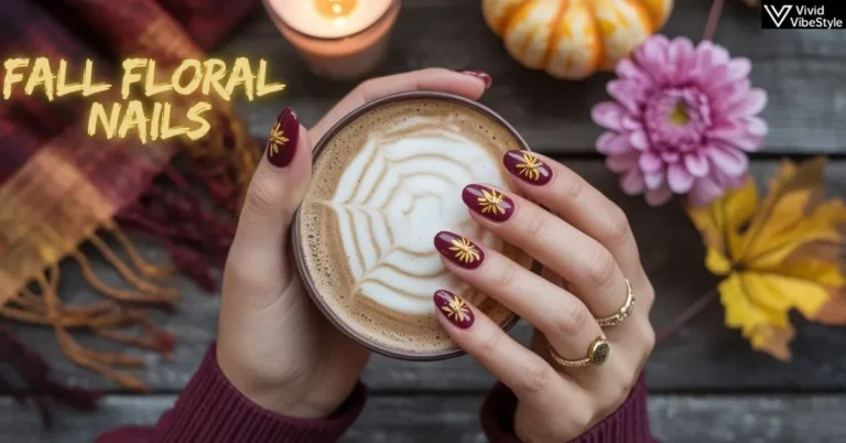 Hands with burgundy fall floral nails featuring gold chrysanthemum designs, holding a pumpkin spice latte, styled with autumn leaves and a cozy scarf